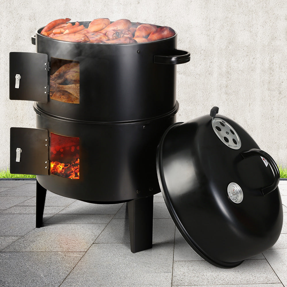 Black Kettle drum style BBQ, Smoker and outdoor Oven combination with cooking food and hot coals glowing red.