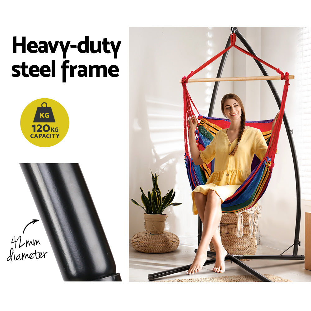 A smiling lady sitting and swinging in a rainbow coloured hammock egg style chair with a self supporting frame.