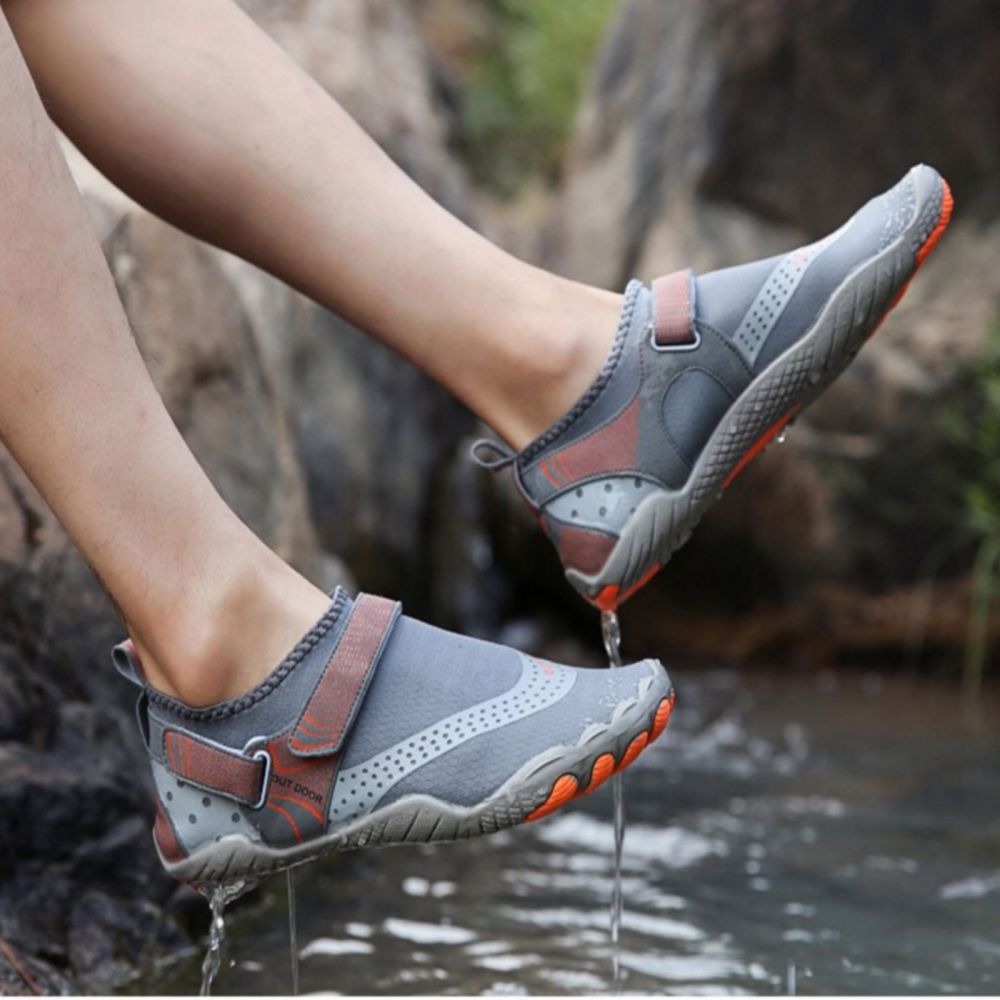 Pair of ankles and calves in grey with orange sole outdoor walk in water shoes dripping water over a river.